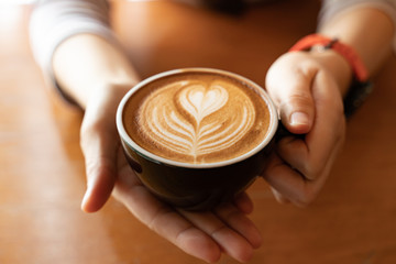 Close up Cup of coffee latte in coffee shop.Female hands holding a cup of coffee cup with heart...