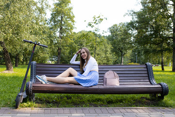 Girl resting on a bench in the park after a trip to the electric scooter