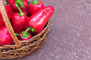  Red (sweet) bell peppers in a wicker basket on a brown background. Copy space.