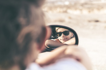 Portrait of beautiful boy looking in the car's mirror. Close up of a caucasian teen with sunglasses and arms crossed. Cool teenager  looking in camera. Youth, positive, travel, freedom concept.