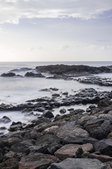 Fototapeta na wymiar Mesa del mar volcanic pebbles coastline, long exposure photography, with Atlantic ocean waves, horizon with sunset light, Tacoronte, Tenerife, Canary islands, Spain