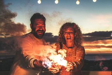 Smiling couple making party with fireworks outdoor in terrace. Happy girl and boy having fun...