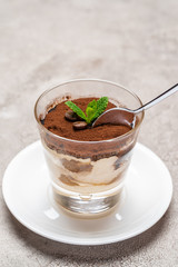 Portion of Classic tiramisu dessert in a glass cup on concrete background