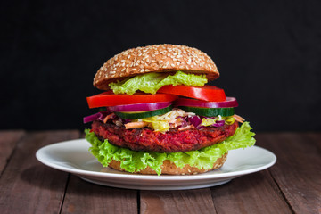 healthy vegan burger with beet patty coleslaw salad cucumber tomato lettuce on plate on dark wooden background 