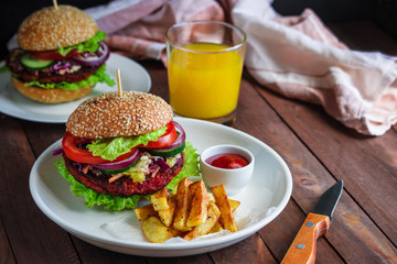 healthy vegetarian burger with beet patty coleslaw salad fresh vegetables fries potato and bowl with tomato sauce glass of orange  juice knife on wooden table