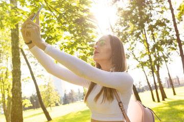 Portrait of a girl who takes a selfie in the Park in the beautiful at sunset