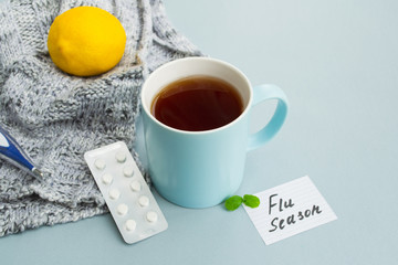 Cold and flu season. Cup with hot tea, lemon, mint, thermometer and tablets on a light background....