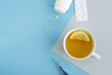 Cold and flu season. Cup with hot tea and lemon, thermometer, pills on a light background....