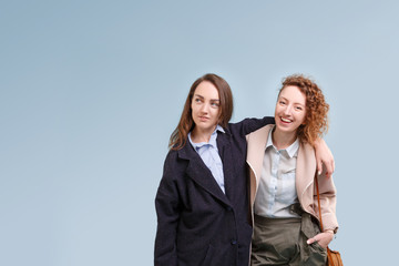 Two positive girls student girlfriends in autumn clothes posing on a blue background. Charming girls selling discounts in a cafe. Copyspace
