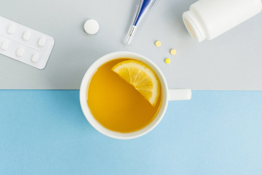 Cold and flu season. Cup with hot tea and lemon, thermometer, pills on a light background. Treatment and prevention of the virus. Copy space