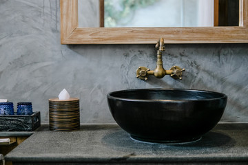 Black sink, vintage copper faucet, gray wall, mirror, loft bathroom interior details. Close up,...