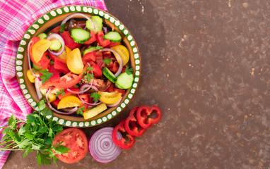 Salad of tomato, pepper, cucumber, onion, herbs. Homemade food. The concept of tasty and healthy food. Dark brown background. Top view. Copy space.