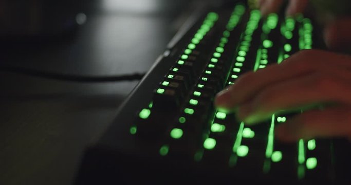 Hands Typing on Gaming Keyboard Glowing Green in Dark Room 