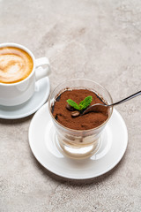 Portion of Classic tiramisu dessert in a glass cup and espresso coffee on concrete background