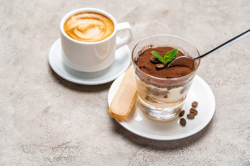 Portion of Classic tiramisu dessert in a glass cup and espresso coffee on concrete background