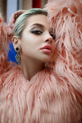 Beautiful girl posing on the street in pink fake fur coat near bright multicolore wall