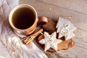 Mug of tea, Christmas gingerbread glazed cookies, cinnamon at wooden background with glares. Cozy tea time with homemade sweets and cup of hot beverage. Winter food, drink, new year lights
