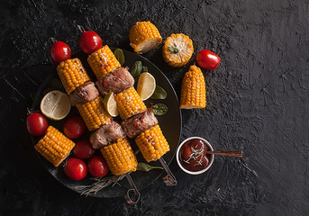 Shish kebab of corn and meat on a black dark background. Fried vegetables. Corn, onion, tomato, pepper. Roasted meat. Grilled vegetables. Copy space. Top view
