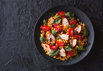Mexican salad with vegetables and chicken on a black dark background. Corn, tomatoes, peppers, beans. Taco mix. The view from the top. Copy space