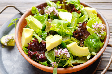 Clay dish with salad of avocado, green and violet lettuce, lamb's lettuce and oregano flowers on vintage metal tray