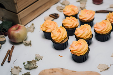 Autumn yellow and orange cupcakes on a light background with autumn dead leaves, pumpkins and apples. Autumn sweets with cream for children. Carrot cupcakes on autumn background.