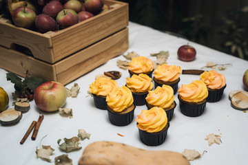 Autumn yellow and orange cupcakes on a light background with autumn dead leaves, pumpkins and apples. Autumn sweets with cream for children. Carrot cupcakes on autumn background.