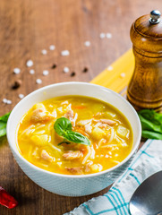 Chicken soup with noodles and vegetables in white bowl on wooden table background