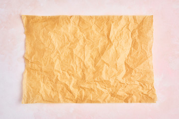 Crumpled piece of brown parchment or baking paper on rose and white texture pattern background. Top view. Copy space for text and design element.