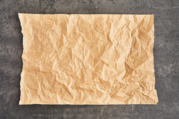 Crumpled piece of brown parchment or baking paper on black concrete background. Top view. Copy space for text and design element.