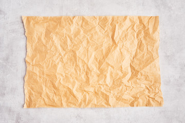 Crumpled piece of brown parchment or baking paper on grey concrete background. Top view. Copy space for text and design element.