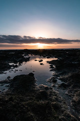 Naklejka premium atardecer frente a un charco de agua con nubes y rocas