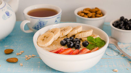 Breakfast. Oatmeal with bananas, strawberries, nuts and blueberries on the blue wooden bakground. Healthy breakfast. Close-up