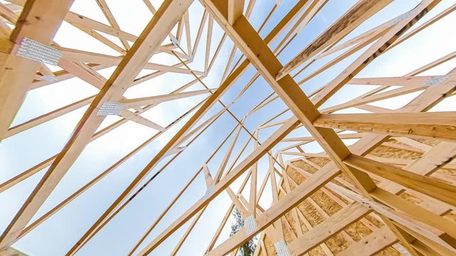4k time lapse clip of wood roof beams of a new home construction site under blue sky and clouds passing by