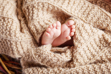 Fototapeta na wymiar Closeup picture of newborn baby feet on beige knitted plaid. Fine concept of the childhood and motherhood