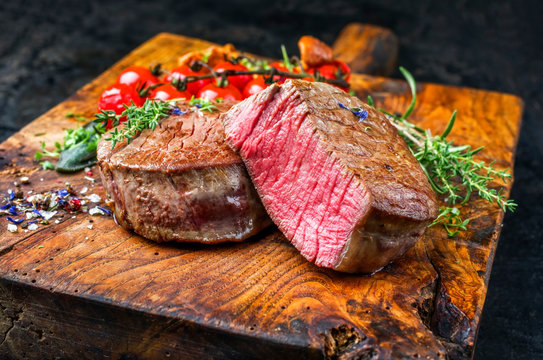 Gebratene dry aged Rinderfilet Steak Medallions  natur mit Tomaten und Pfifferlinge als closeup auf einem rustikalen Holz Schneidebrett