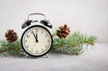New Year and Christmas concept. Black alarm clock and fir branches on a gray concrete background.