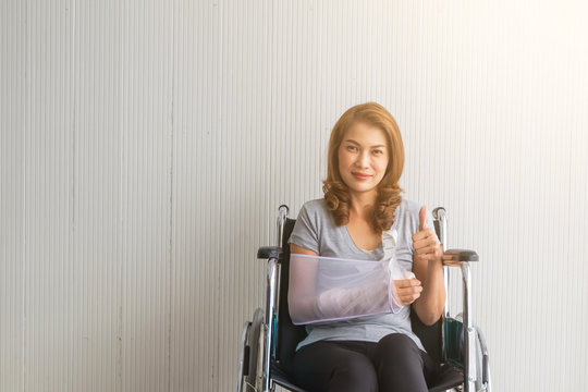 Broken arm Asian woman with arm sling sponsored in her hands sitting on a wheelchair Ideas for accident Injuries and health care Studio shot on a white background.