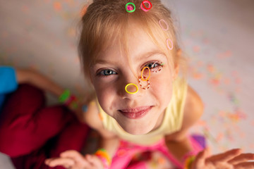 happy kids, a boy and a girl, 7-8 years old are engaged in hobbies, weave colored bracelets from rubber bands together, a mess, poured elastic bands on the face