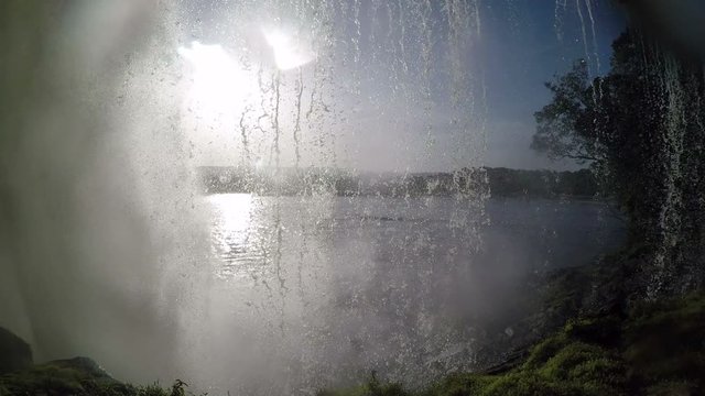 A view behid a raging and roaming waterfall in Canaima national park in Venezuela. Water is falling and the sun is shining.