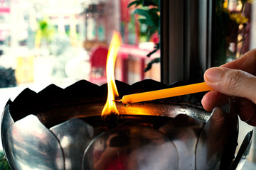 Faith and religious.Man hand holding yellow candle getting fire  from big oil lamp in chinese shrine.