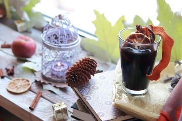 Cup with mulled wine, autumn leaves, seasonal fruits and vegetables, decor, spices on a window background, home comfort concept