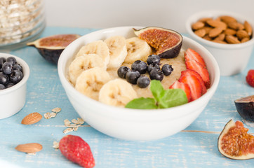 oatmeal with blueberries, strawberries, figs, banana and almonds. Healthy breakfast on a wooden blue background. 