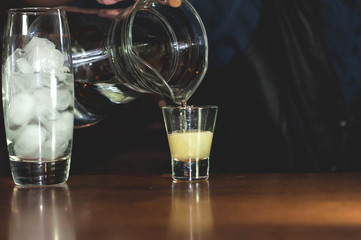 selective focus of barman hands  pouring clear liquid into glass with lemon juice decanter into glass with alcohol cocktail and ice cubes on bar counter in restaurant