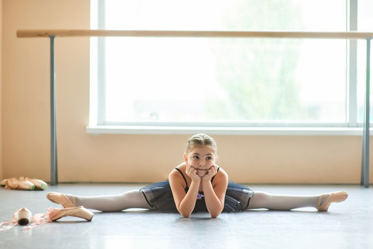 Beautiful ballet dancer in black dress. Slim pretty young girl athlete sitting on the split in ballet class.