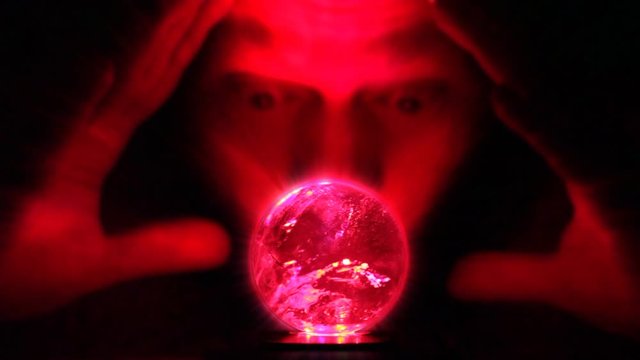 A man looks into a glowing ball of glass looking for divination of the future.