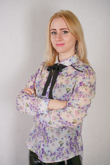 Beautiful young blonde woman in a floral blouse with a bow posing in white studio