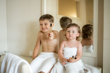 Cute little girl in a bath towel on the head and a bathrobe cleaning teeth in the bathroom against the mirror