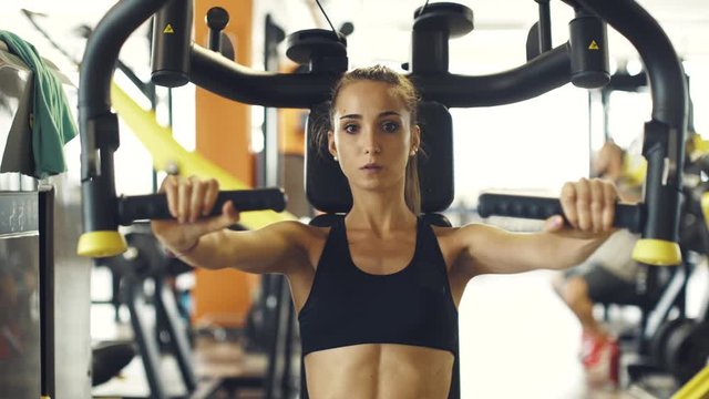 Young sporty woman exercising on a pec deck machine