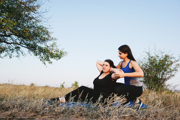Obese woman doing sit-ups with personal trainer