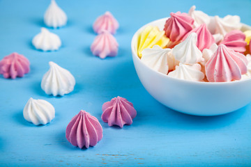 Tasty white and pink meringues on a blue wooden background.